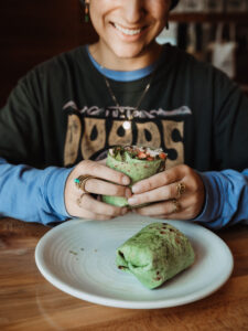 Person holding a green veggie wrap above a plate